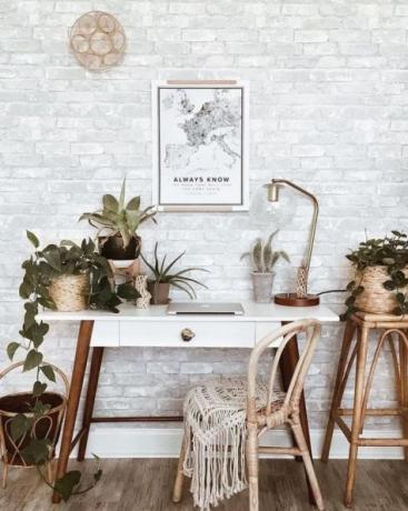 Šiks boho mājas birojs ar retro koka galdu, boho paklāju, sienas mākslu, daudz istabas augu: kaktusi un sukulenti